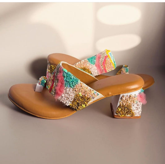 Pair of tan high-heeled shoes with colorful floral embellishments on a neutral background