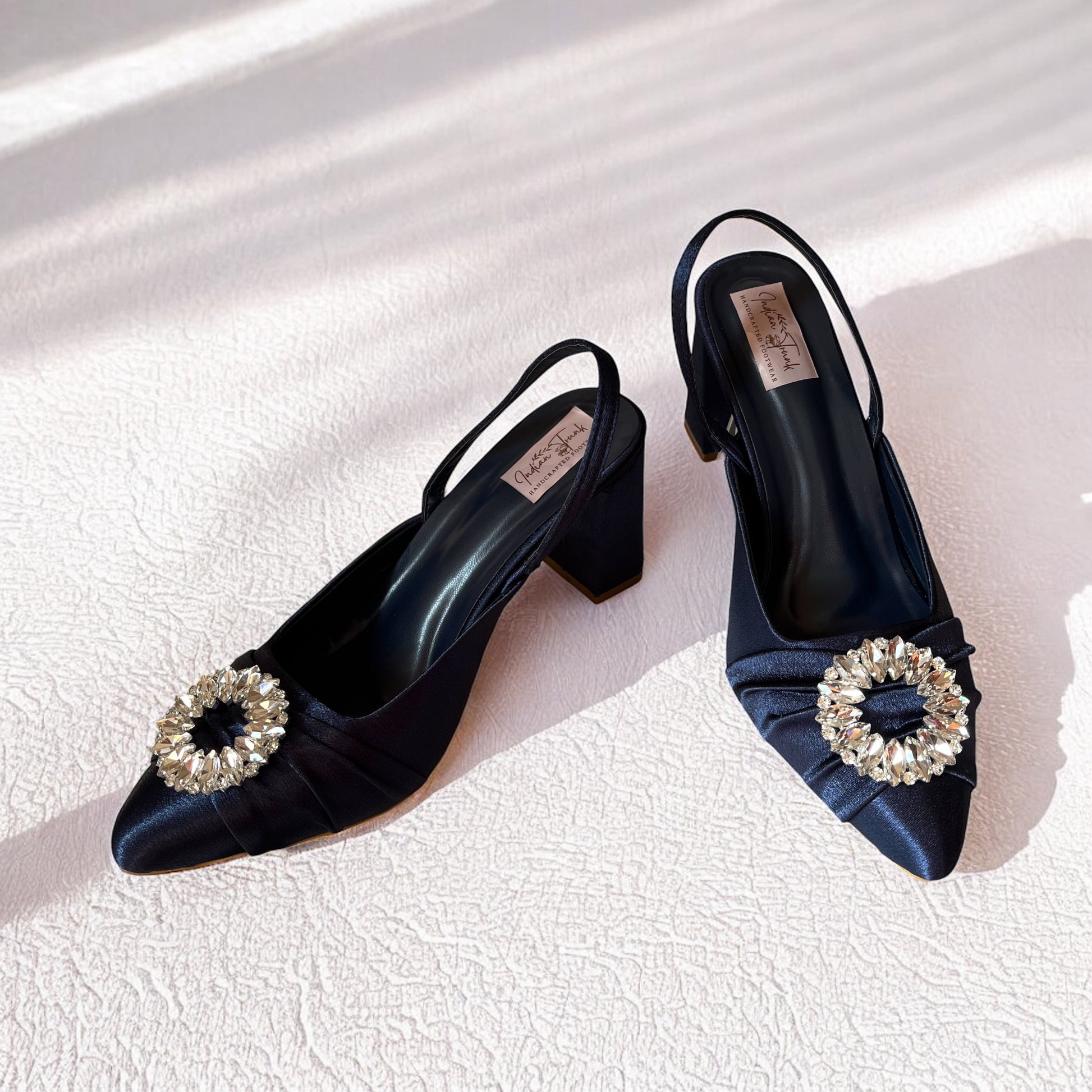 Navy blue high-heeled shoes with decorative embellishments on a light background