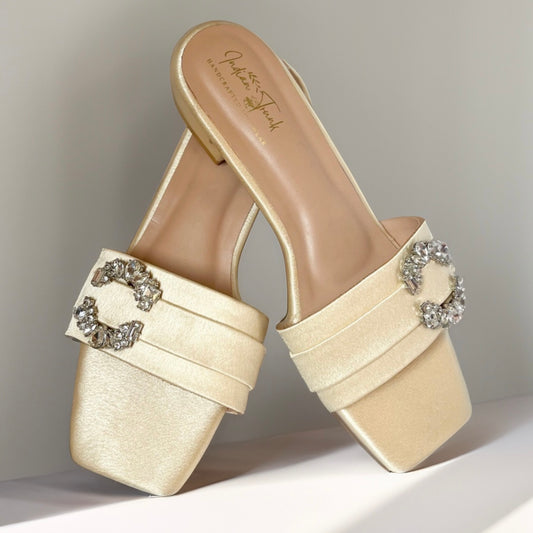 Beige high-heeled shoes with decorative embellishments on a neutral background